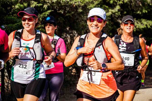 Group of women competitors running together wearing sports hats and camelback hydration backpacks.